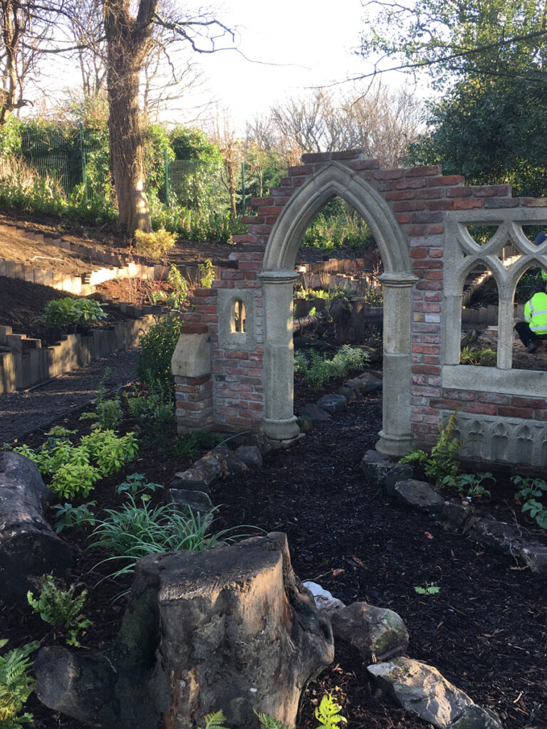 Planted garden beds surrounding a stone archway feature