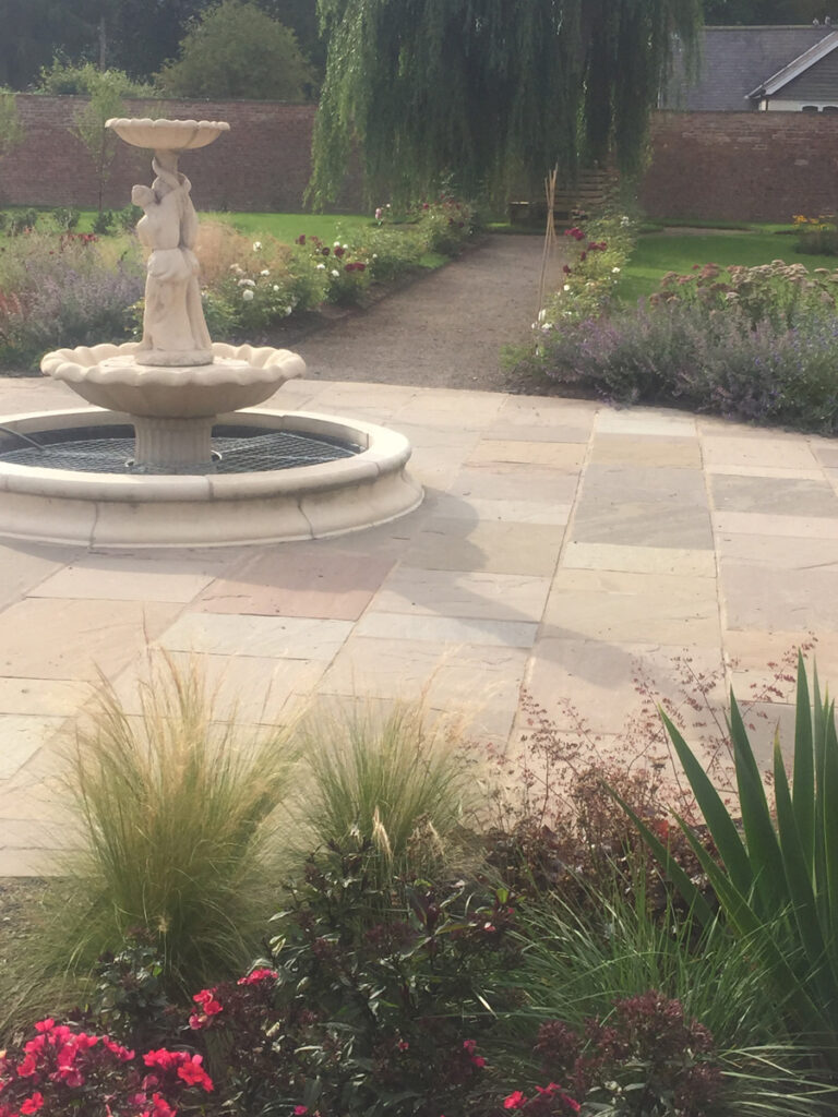 Fountain in the centre of a flagstone feature surrounded by flower beds